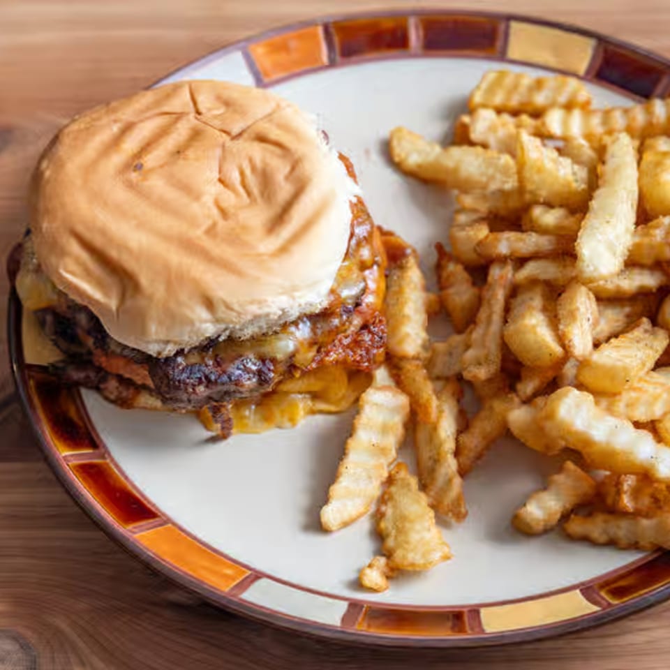 A double cheeseburger with melted cheese and crinkle-cut fries on a patterned plate.