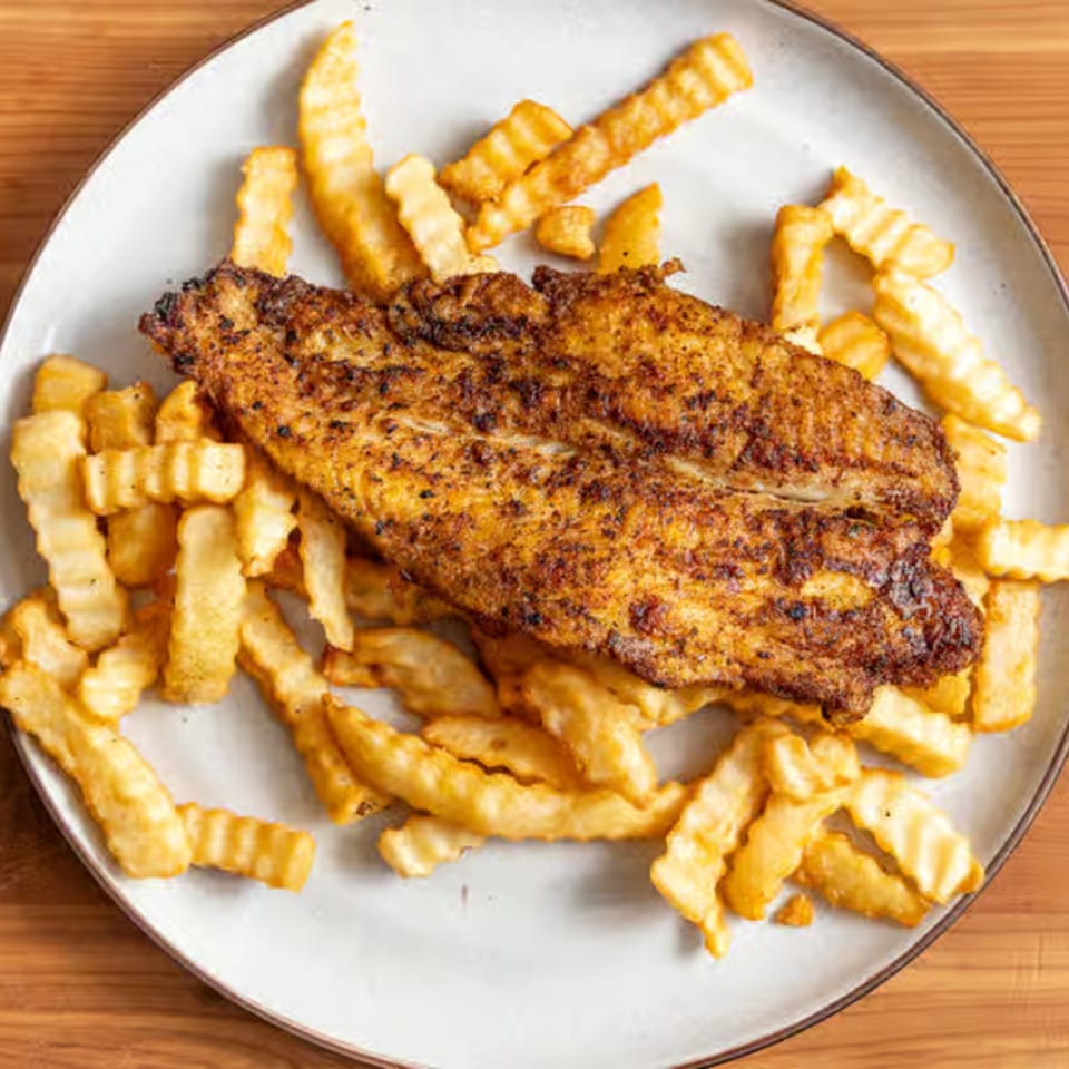 A plate of golden-brown fried fish fillet seasoned with spices, served with crinkle-cut french fries.
