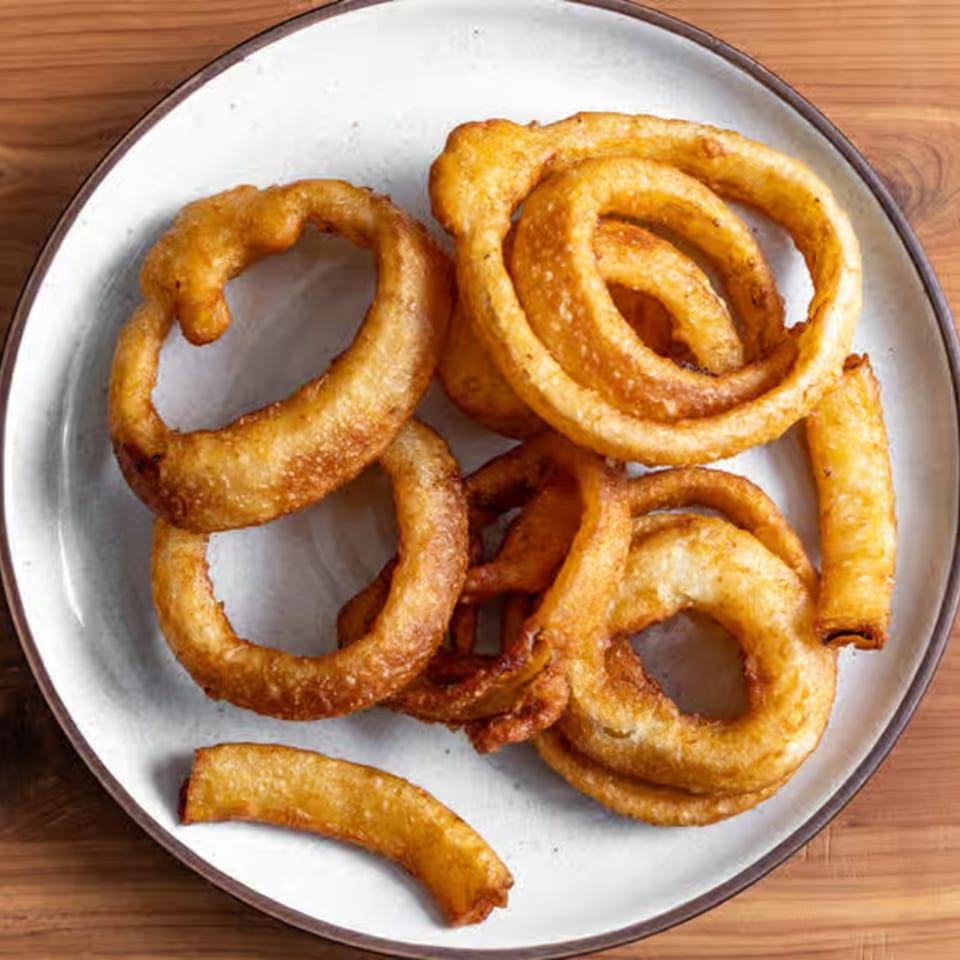 A white plate filled with golden-brown, crispy curly fries and onion rings on a wooden table.