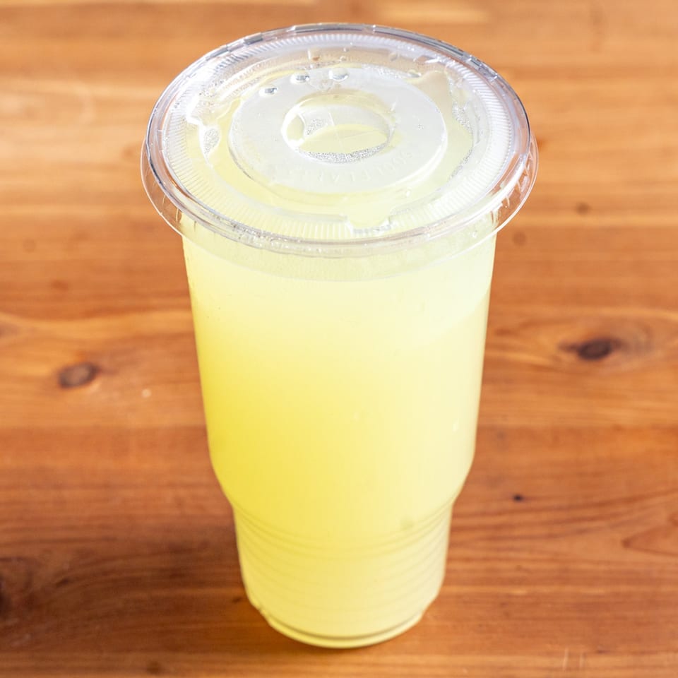 A clear plastic cup of Oh' Lemonade with a lid, sitting on a wooden table.
